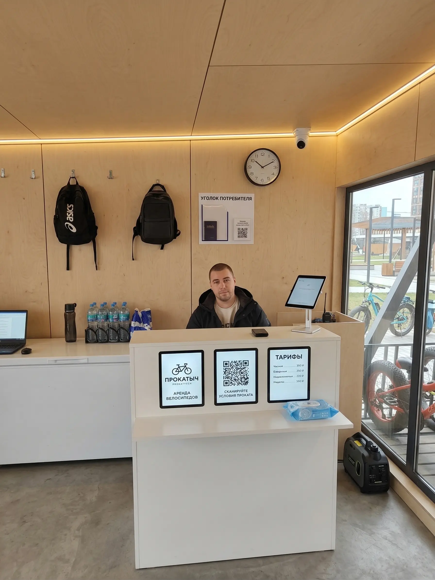 Касса BIWLS на острове Татышев: оператор за стойкой оформляет аренду транспорта, на стойке размещены QR-код с условиями проката и тарифы